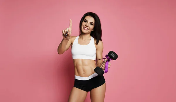 Atlético muscular fitness mulher fazendo exercício para os braços com grande haltere trabalhando em rosa apontando dedo para cima — Fotografia de Stock