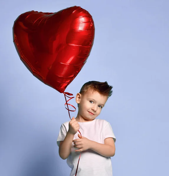 Маленький хлопчик любить тримати велику червону серцеву кульку, щоб відсвяткувати день валентинки на фіолетовому — стокове фото
