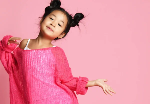 Азіатський дитина дівчина в рожевий светр, білі брюки і смішні булочки знаходиться в позі моди і посміхається. Безплатне текстове простір — стокове фото