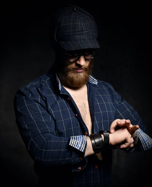 Бородатый мужчина в клетчатой рубашке и клетчатой кепке посмотрите на его наручные часы — стоковое фото