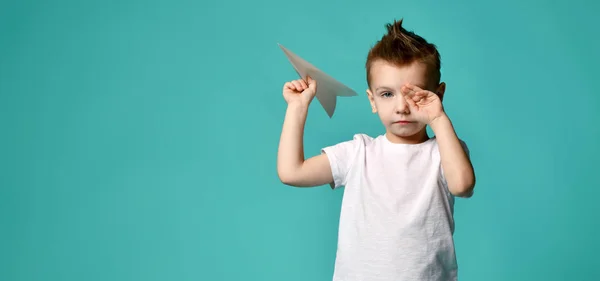 Niño listo para lanzar un avión de papel, pero se detuvo a frotar el ojo con la mano. nuevo paso. un comienzo difícil. espacio libre de texto —  Fotos de Stock