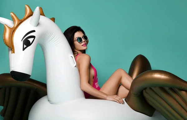 Young fashion woman relaxing with big inflatable unicorn pegasus float mattress in sexy pink bikini for swimming pool — Stock Photo, Image