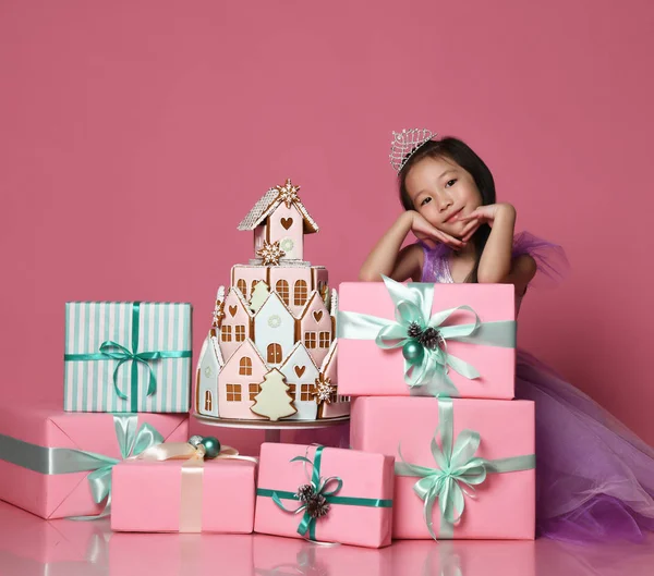 Piccola ragazza asiatica in corona e vestito viola con molte scatole regalo presenti e biscotti allo zenzero festa di compleanno torta — Foto Stock