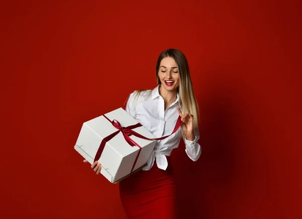 Jovem loira segurar caixa branca presente sorrindo tentar abri-lo na festa de aniversário celebração no vermelho — Fotografia de Stock