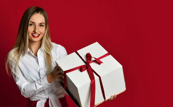 Giovane donna bionda tenere scatola bianca regalo sorridente cercare di aprirlo sulla festa di compleanno celebrazione sul rosso — Foto Stock