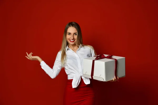 Giovane donna bionda tenere scatola bianca regalo sorridente dito puntando la mano all'angolo — Foto Stock