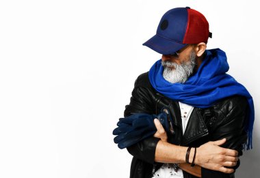Old brutal senior rich man in leather jacket blue and red baseball cap and long blue scarf stands with gloves in arms stylish fashionable men  clipart