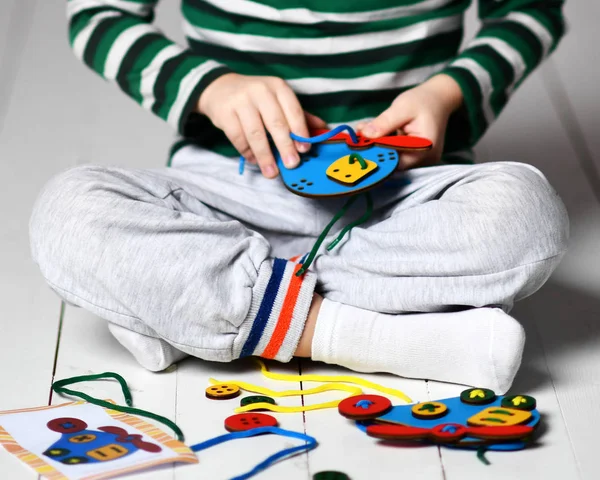 Kid boy plays educational game interestedly with wooden colorful helicopter and laces — Stock Photo, Image