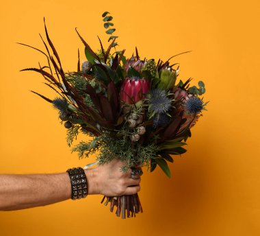 Adam elini tut thistle eryngium sarı zemin üzerine modern gelin buketi egzotik çiçekler yeşil yapraklar