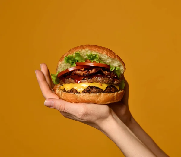 Kobieta ręce trzymać duże dwukrotnie cheeseburger sandwich burger z wołowiny i boczek na żółty — Zdjęcie stockowe