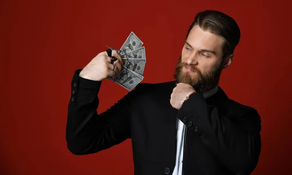 Stylish bearded business man holding American dollars banknotes thinking and is intrigued on red — Stock Photo, Image