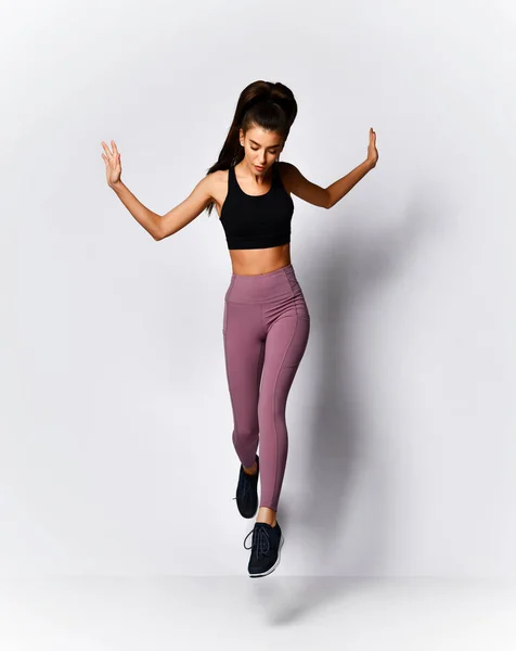 Mujer morena delgada corriendo saltando haciendo ejercicio de entrenamiento en ropa deportiva en gris —  Fotos de Stock