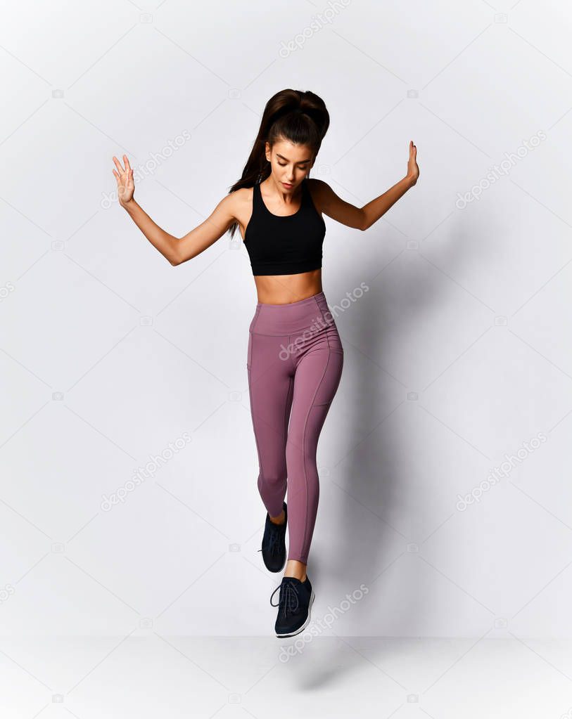 Slim brunette woman running jumping doing  workout exercise in sport wear on gray 