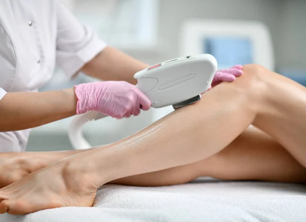 Fecha a porta. Médico-cosmetician em luvas realiza um procedimento na perna do paciente com laser de equipamentos médicos no salão de beleza equipado — Fotografia de Stock