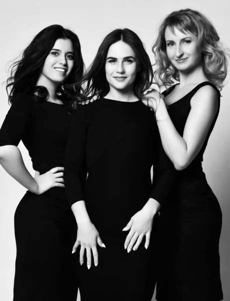 Three friends stylish young women in black tight midi dresses are are going to the dinner party. Black and white