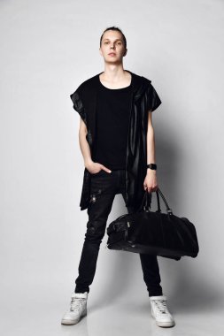 Siyah kot pantolon, t-shirt, uzun kolsuz ceket, beyaz spor ayakkabı ve büyük bir modern çanta ile baş bir topuz ile uzun boylu şık adam