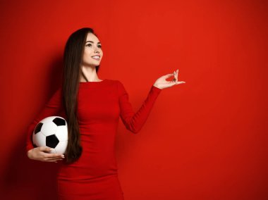 Young smiling brunette woman in tight red dress with soccer ball in her hand looks up dreamly and calculates winnings clipart