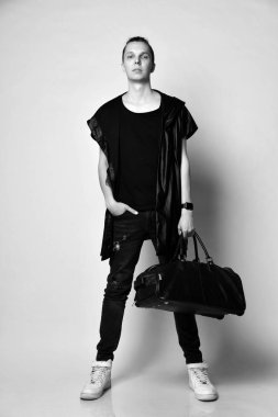 Siyah kot pantolon, t-shirt, uzun kolsuz ceket, beyaz spor ayakkabı ve büyük bir şık çanta ile baş bir topuz ile şık adam