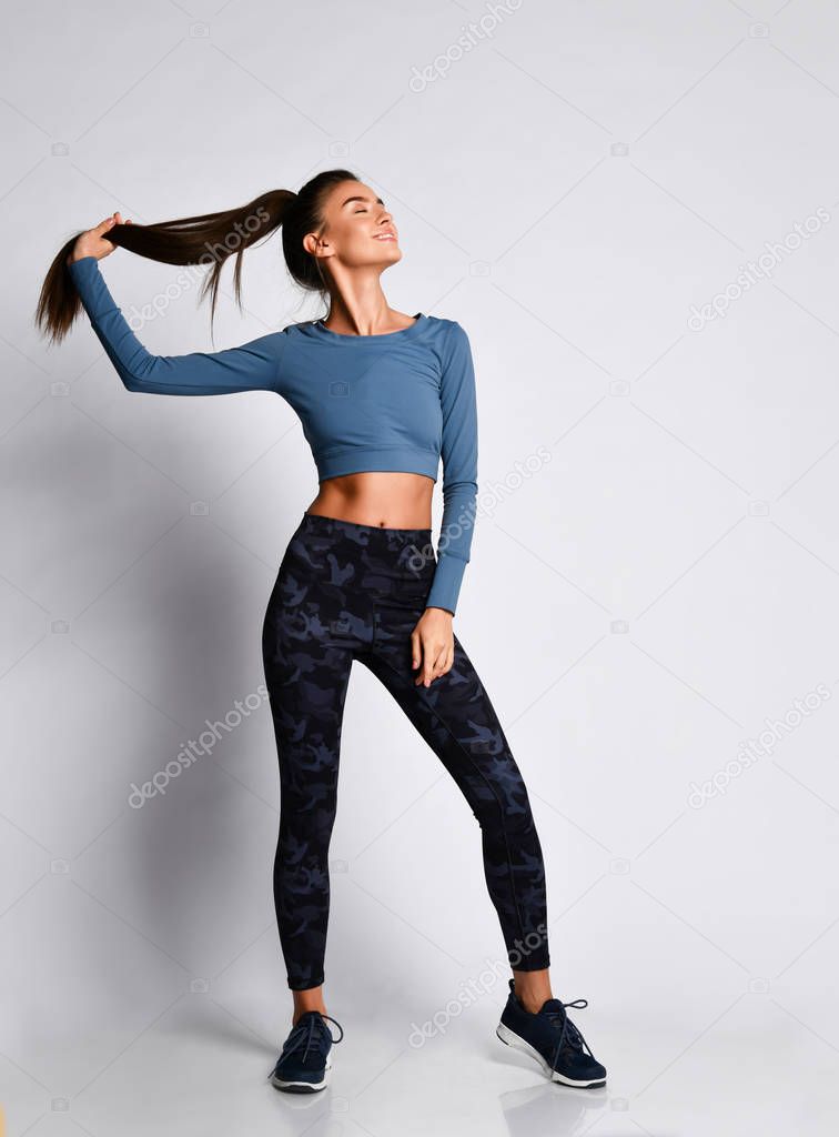 Sporty slim brunette fitness woman during workout exercise in purple sport wear on gray full body