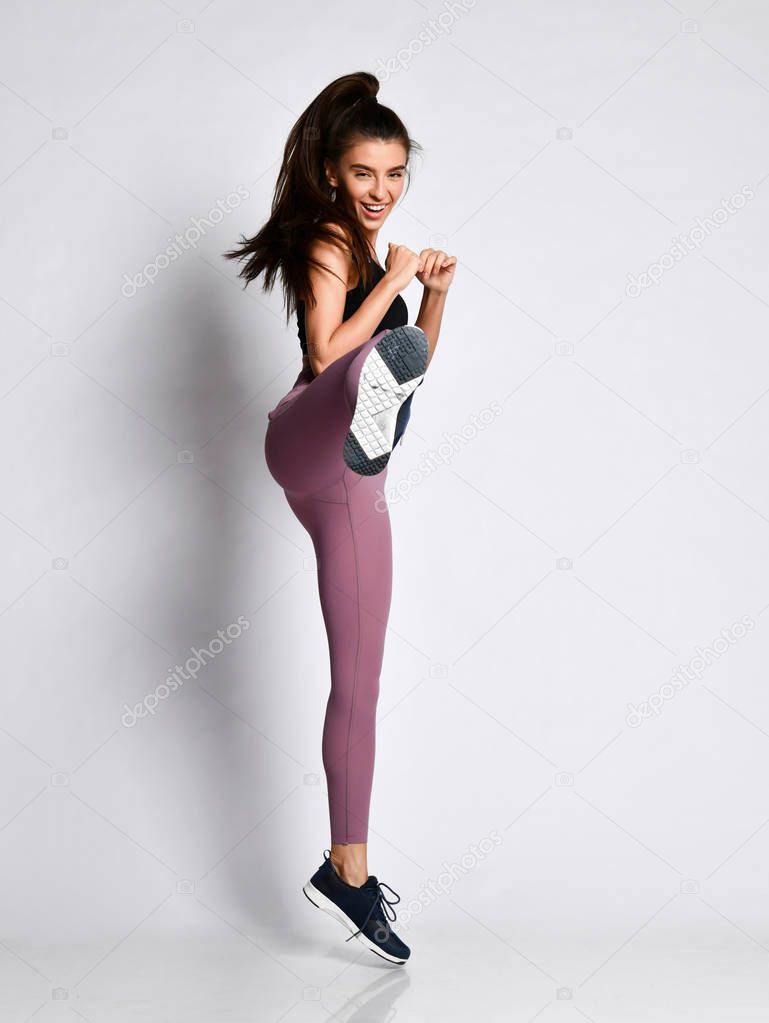 Young sporty girl in sportwear fighter kicking with the leg hit in sport wear cloth on gray 
