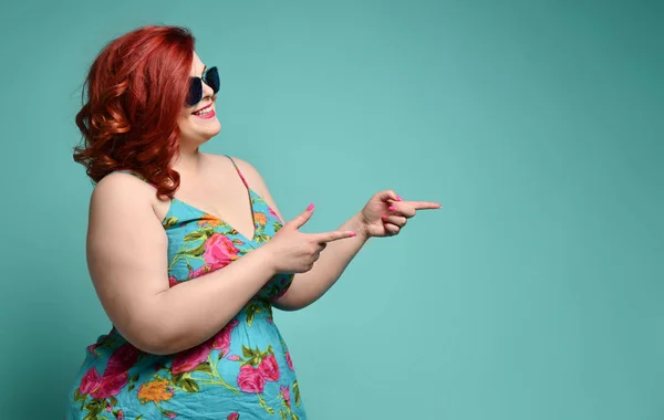 Plus-size overweight redhead lady in sunglasses shows a gesture sign finger - gun, aimed at free text copy space on mint