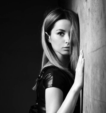 Genç, güzel esmer, siyah, modern, deri kumaşlı kadın siyah duvara yaslanıyor. 