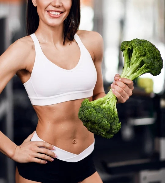 Gros plan. Régime alimentaire et concept de perte de poids. Femme sportive instructeur de fitness avec abdos parfaits en costume de gym avec un gros brocoli comme poids — Photo