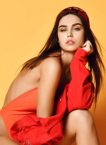 Fiatal divat szexi nő piros modern fürdőruha és kabát viselet sapka ül pózol sárga — Stock Fotó