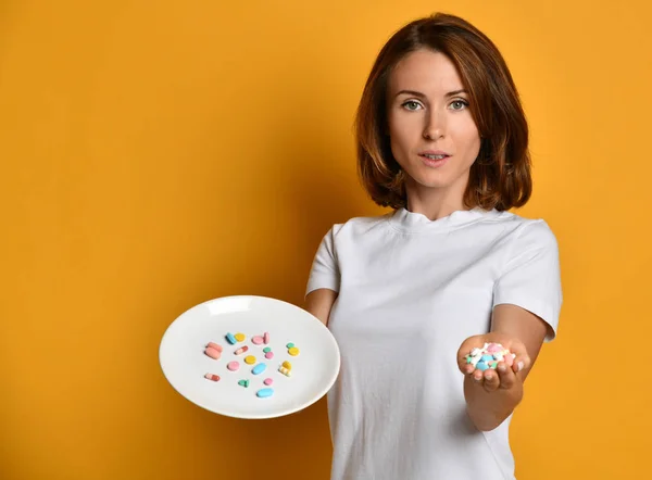 Woman nutritionist hold a white plate with different color tablet pills diet supplements prescription weight loss drugs on yellow — Stock Photo, Image