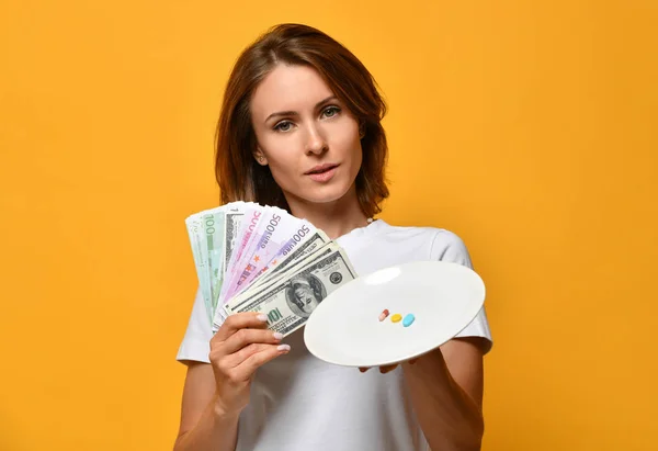 Ernährungswissenschaftlerin halten Teller mit verschiedenen Farben Tabletten Nahrungsergänzungsmittel verschreibungspflichtige Medikamente und Dollar Geld Währung auf gelb — Stockfoto