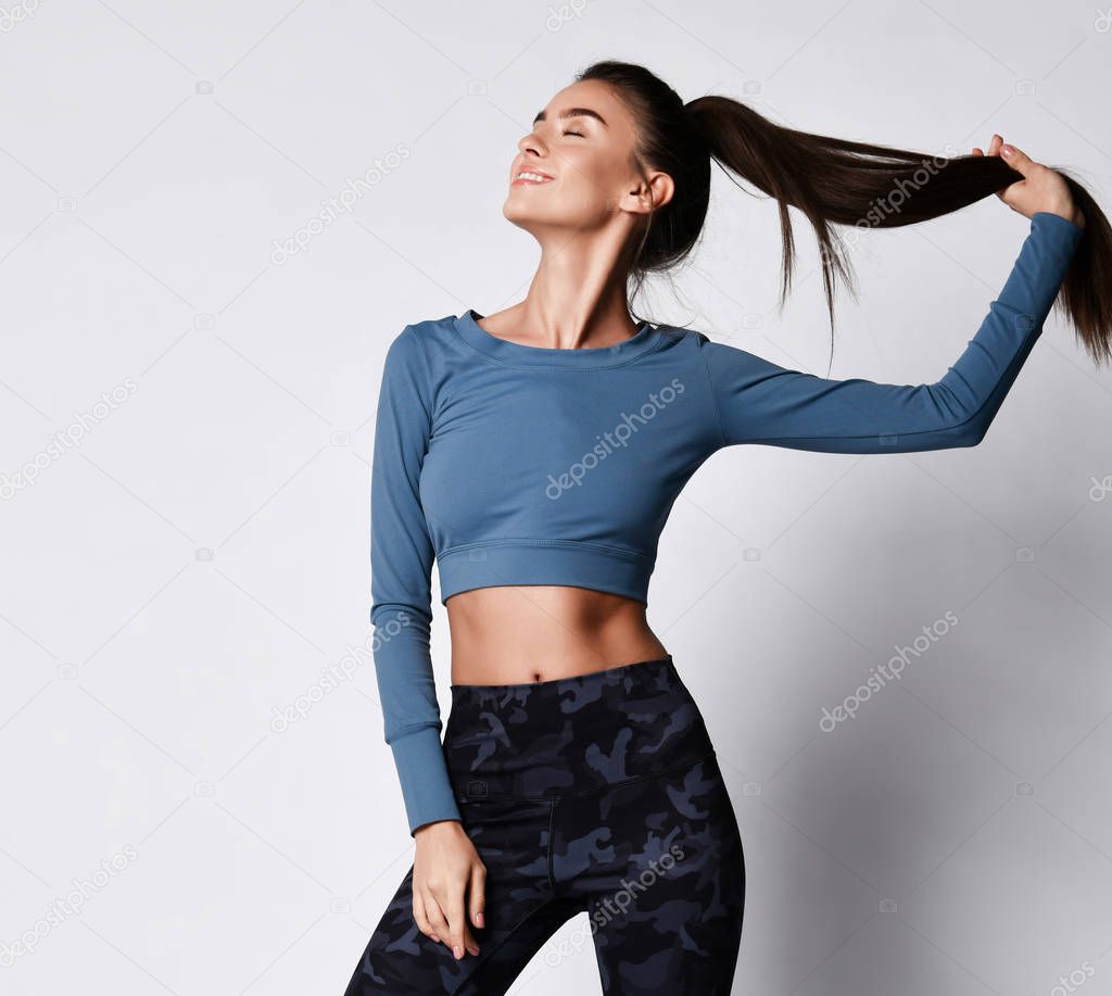 Sporty slim brunette with ponytail fitness woman enjoys workout exercise in purple sport wear on gray