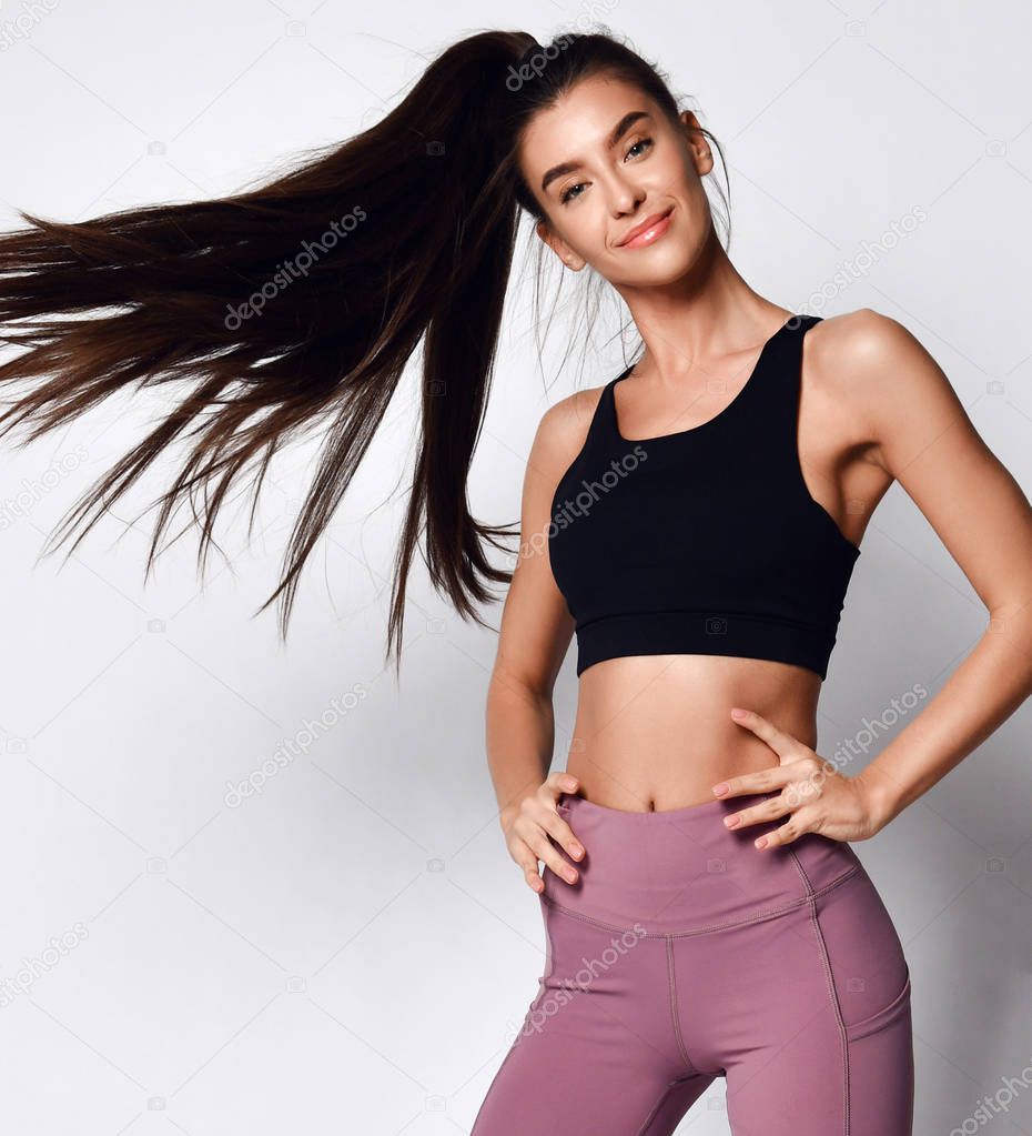 Sporty slim brunette with ponytail fitness woman enjoys workout exercise in purple sport wear on gray