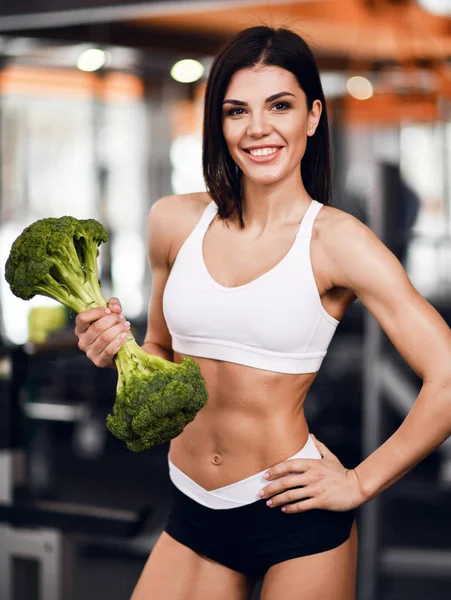 Diéta és fogyás koncepció. Sportos nő fitness oktató ajánlja a megfelelő táplálkozás gazdaság nagy brokkoli, mint a tömeg ostobább — Stock Fotó