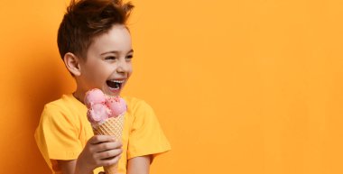 Erkek bebek tut çilek pembe dondurma waffle koni mutlu sarı köşesinde bakarak gülüyor