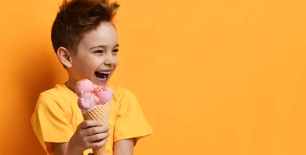 Menino menino segurar morango rosa sorvete em waffle cone feliz rindo olhando para o canto no amarelo — Fotografia de Stock