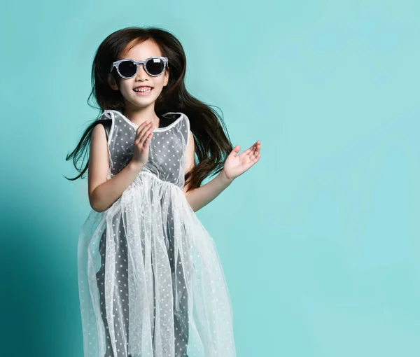 Kleine Aziatische meisje Kid in stijlvolle mode jurk en zonnebril sprongen en klappen haar handen op blauwe Mint — Stockfoto