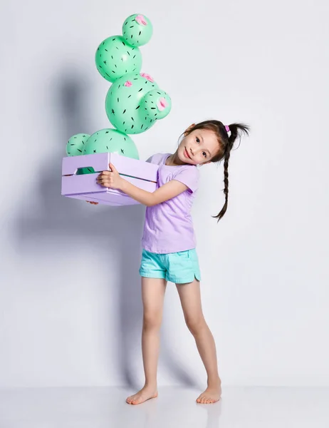 Маленька азіатська дівчинка з однією кумедною косою в синій футболці і шортах несе в собі синю коробку з кактусовою кулею — стокове фото