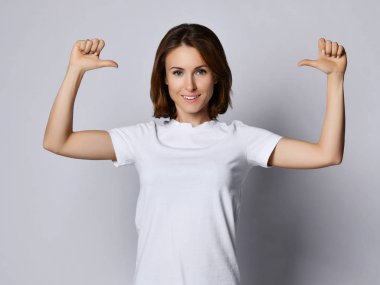 Beyaz tişörtlü mutlu gülümseyen kadın başparmaklarıyla kendini gösteriyor.