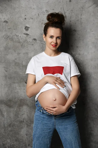 Hermosa joven embarazada feliz madre mujer en camiseta blanca posando en la oscuridad — Foto de Stock