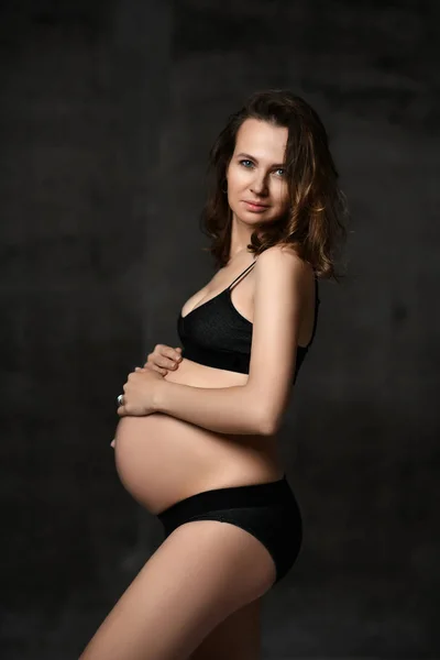 Vacker ung gravid lycklig mamma kvinna poserar i underkläder på Dark — Stockfoto