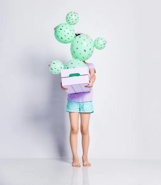 Little girl kid holds a flower box with cactus balloon with pink flowers so it completely hides her face