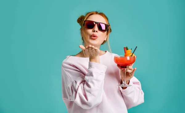 Clubbing jovem mulher moderna na moda óculos de sol mantém um coquetel trópico margarita de morango com uma fatia de laranja envia um beijo — Fotografia de Stock