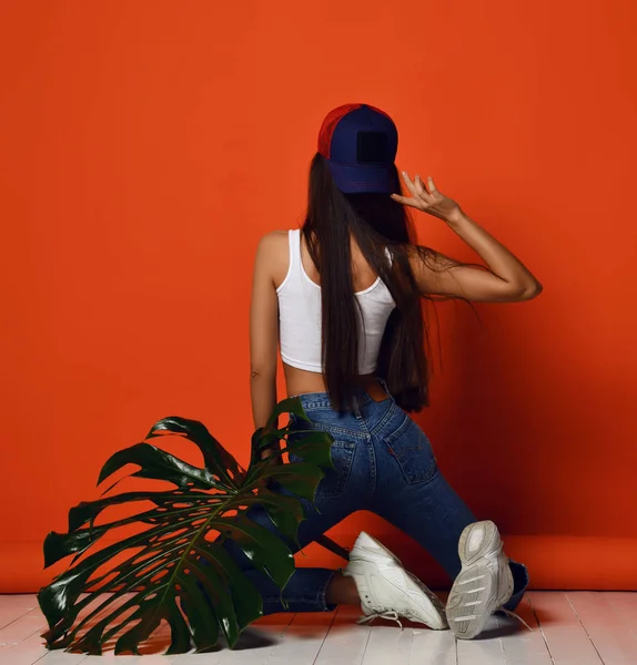 オレンジ色の熱帯の葉の裏側の背面のビューと青い十代の帽子をかぶった若い女性 — ストック写真