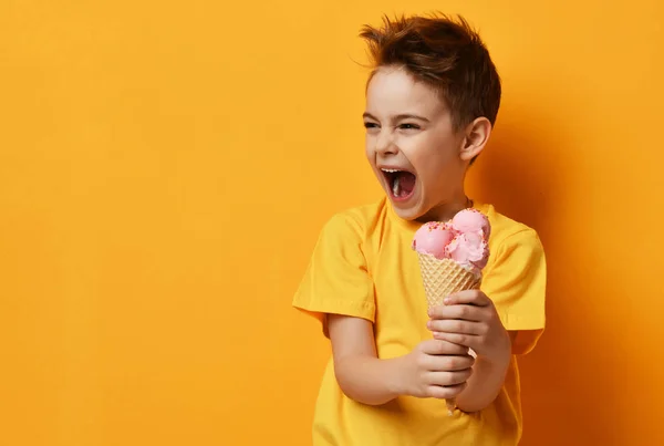 Menino bebê garoto comendo sorvete de morango em waffles cone feliz gritando rindo no fundo amarelo — Fotografia de Stock