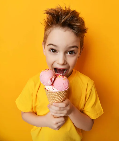Малыш, который ест клубничное мороженое в вафельном конусе, счастлив крича, смеясь на желтом фоне — стоковое фото