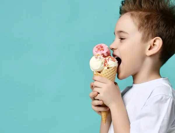 Niño niño sostiene tres cucharadas de helado de fresa y vainilla en gofres cono sobre fondo de menta azul —  Fotos de Stock