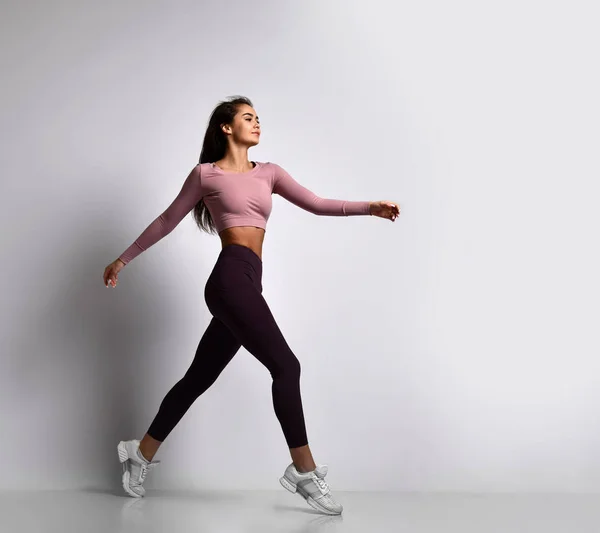 Ung atletisk kvinna brunett flicka i en bra form med hår i en hästsvans i trendiga sportkläder gym Uniform hoppar danser — Stockfoto