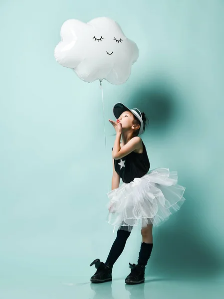 Маленька азіатська дівчинка в модній спідниці тримає металеву хмарну кулю для дітей на день народження і відправляє поцілунок на блакитну м'яту — стокове фото