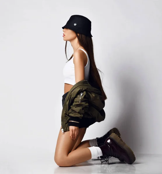 Young beautiful hipster girl sitting on her knees full body in shorts brown spring jacket modern stylish boots and hat — Stock Photo, Image