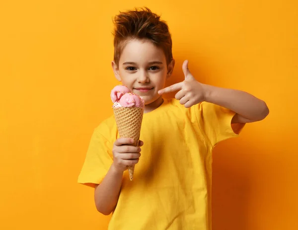 Menino bebê comendo sorvete de morango em waffles cone feliz apontando dedo mostrar polegares para cima no amarelo — Fotografia de Stock